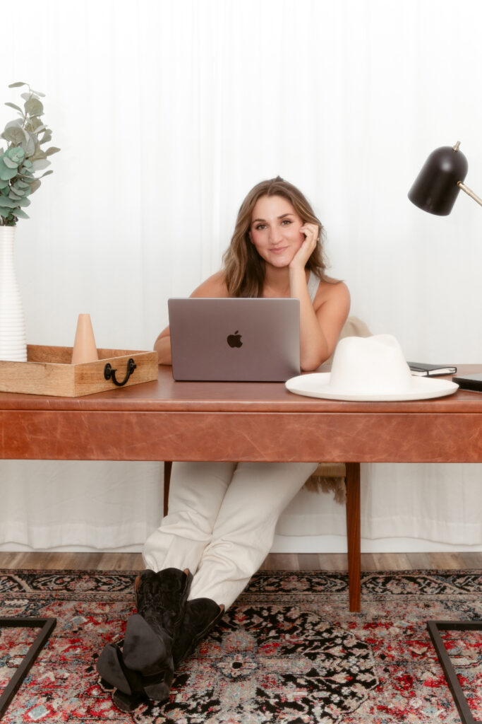 A small business copywriter pauses behind her laptop at a desk, thinking about brand voice copywriting strategy.