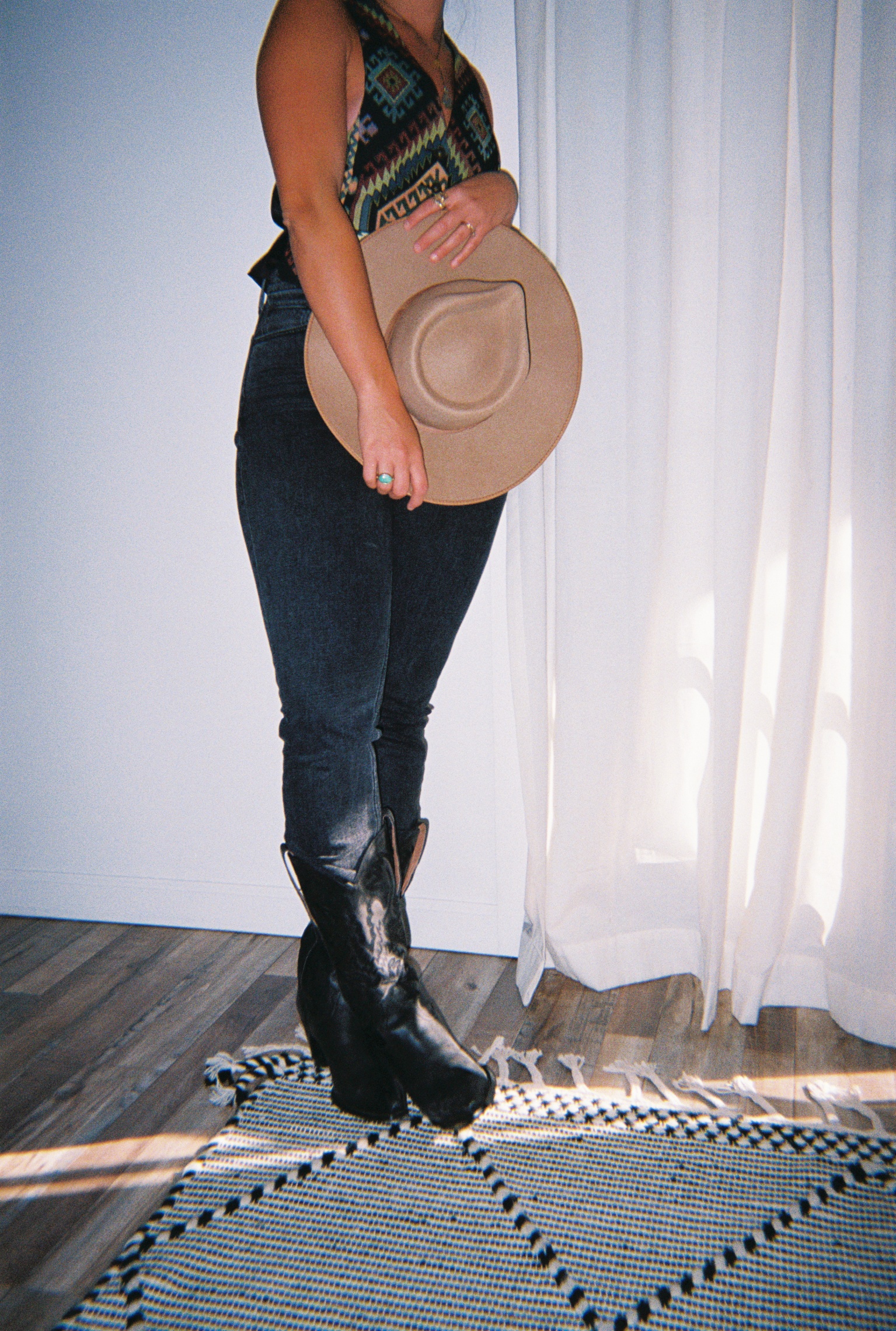 A writer who specializes in evergreen copywriting holds a cowboy hat up against an all black outfit.