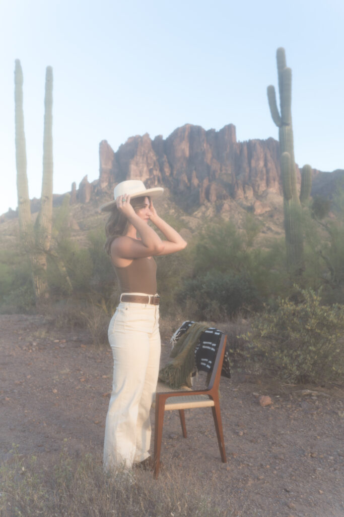 A small business copywriter adjusts her cowboy hat near a cactus in an Arizona desert during her small business brand shoot.