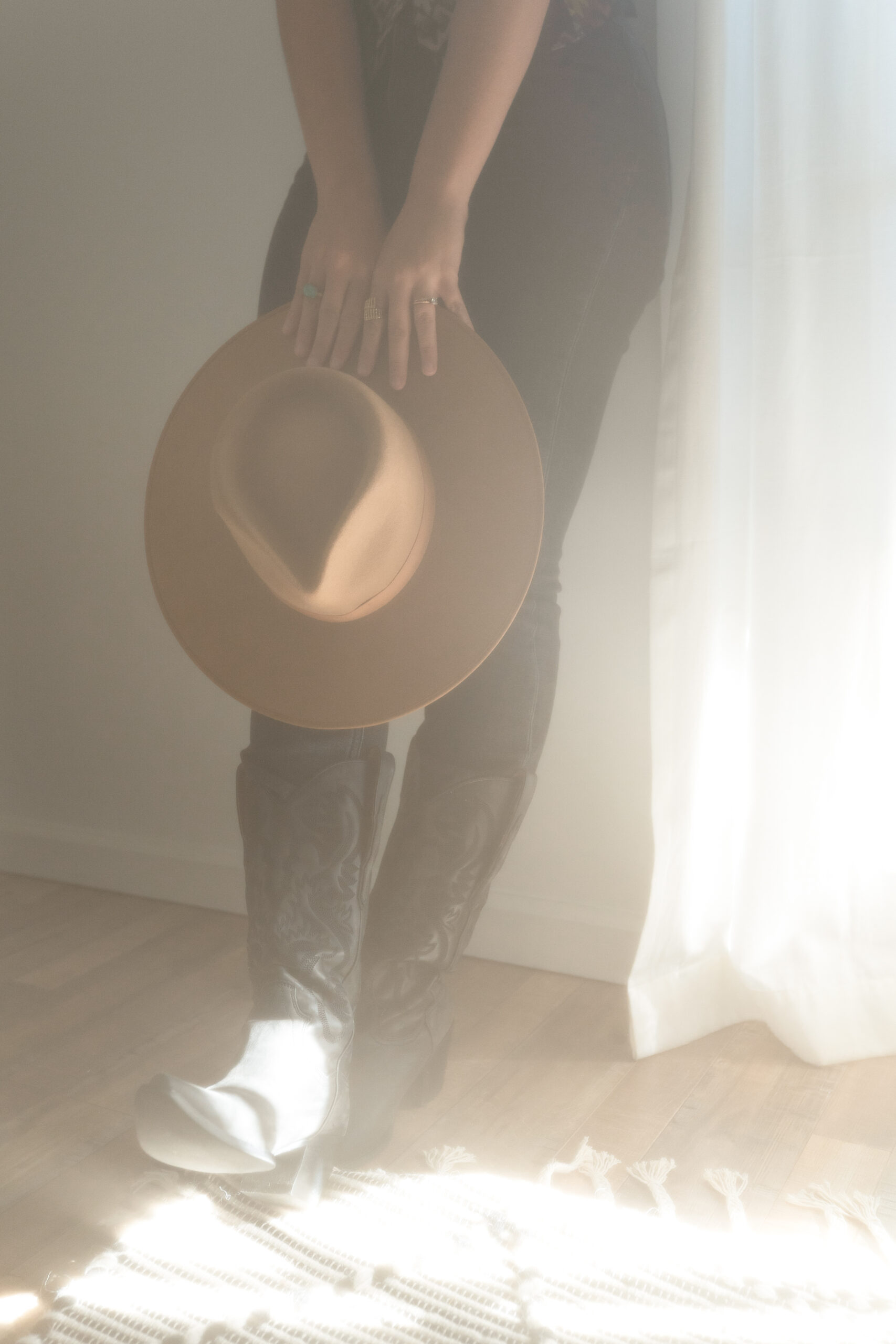 A copywriter holds her hat near her cowboy boots.